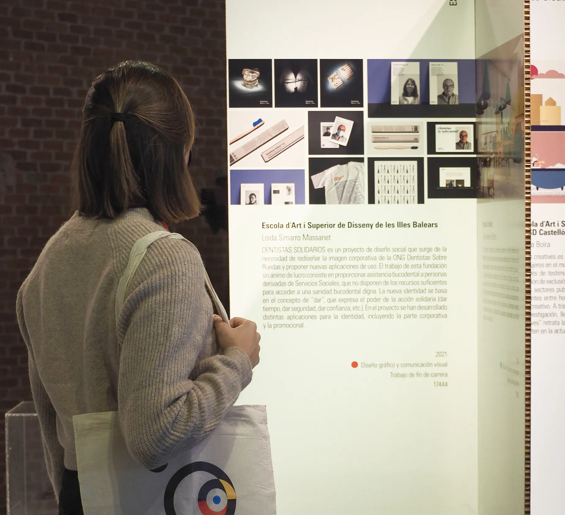 Loida Massanet carrying a "9º Encuentro Bienal Iberoamericana de Diseño - Enseñanza y Diseño" tote bag while observing the "Dentistas Solidarios" project exposition.